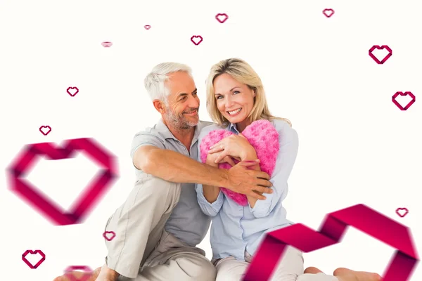 Happy couple sitting and holding heart pillow — Stock Photo, Image