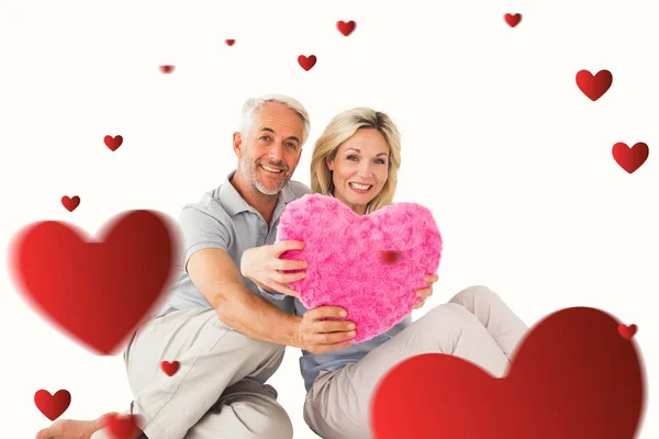 Happy couple sitting and holding heart pillow — Stock Photo, Image