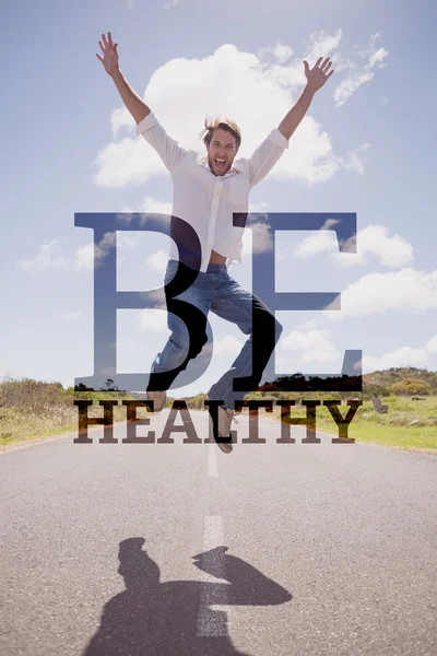 Imagen compuesta de un hombre guapo y casual saltando en un camino sonriendo — Foto de Stock