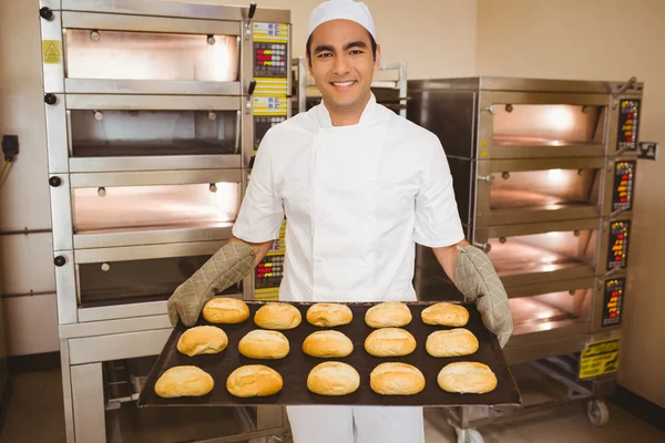 Baker sonriendo a la cámara sosteniendo bandeja de rollos —  Fotos de Stock