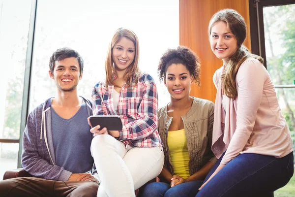 Glada studenter sitter på en soffa med mobiltelefon — Stockfoto