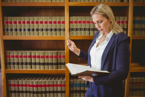 Focused librarian reading book and holding reading glasses — Stock Photo, Image