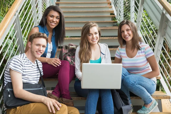 Étudiants souriants assis sur des marches avec ordinateur portable — Photo