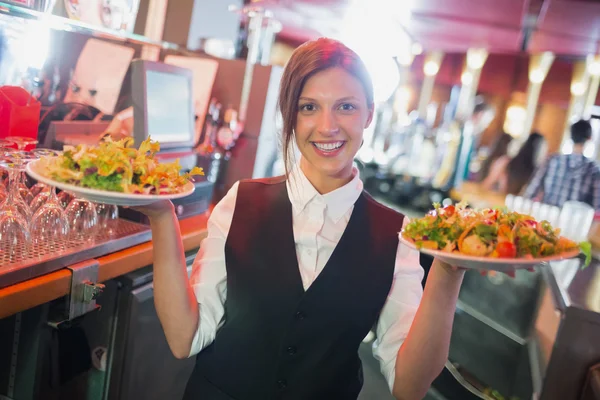 Krásná barmanka drží desky salátů — Stock fotografie