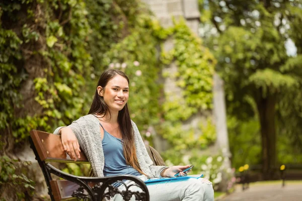 Étudiante souriante assise sur un banc tenant son téléphone portable — Photo