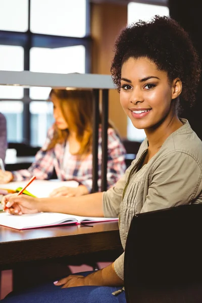 Estudiante sonriente sentado en el escritorio mirando — Foto de Stock