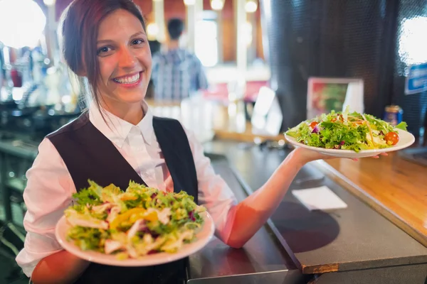 Bonito barmaid segurando pratos de saladas — Fotografia de Stock