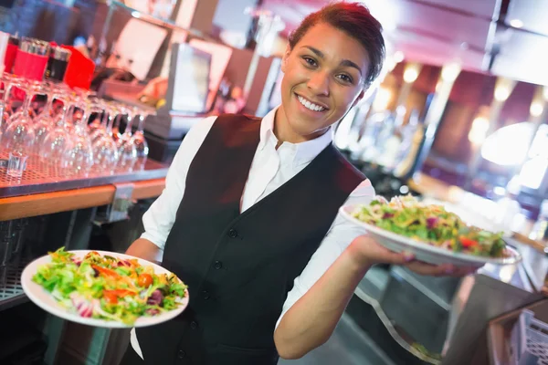 Krásná barmanka drží desky salátů — Stock fotografie