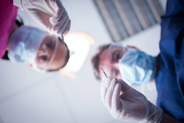 Dentista e assistente inclinados sobre o paciente com ferramentas — Fotografia de Stock