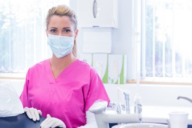Portrait of a dentist in mask looking at camera beside chair clipart