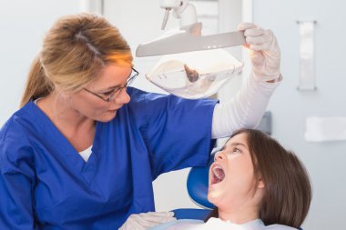 Dentist examining with a light her young patient clipart