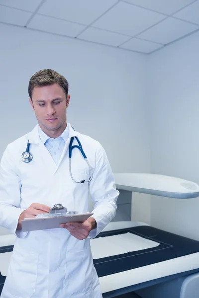 Doctor standing in front of the x-ray machine writing something — Stock Photo, Image