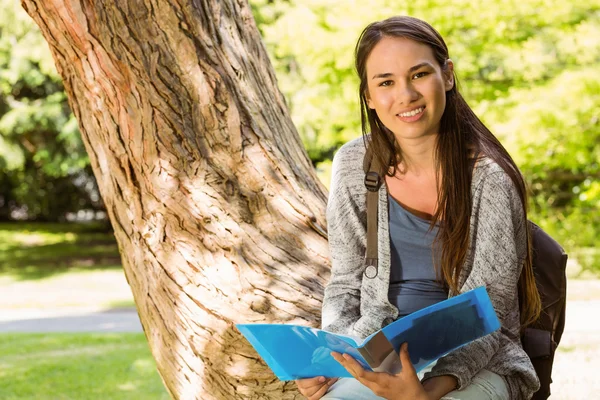 Smiling student sitting on trunk and holding book — Stock Photo, Image
