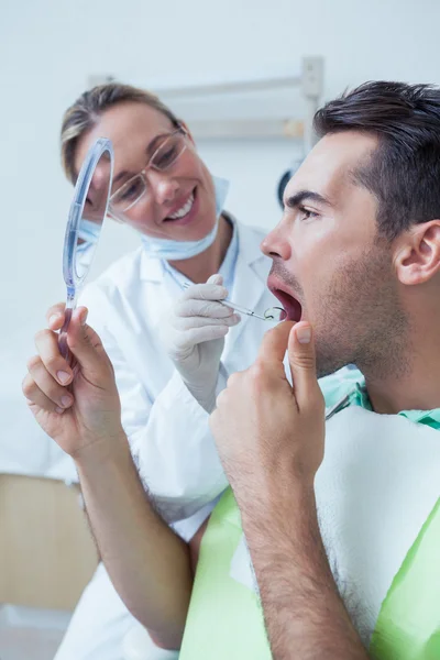 Homem olhando para o espelho pelo dentista feminino — Fotografia de Stock