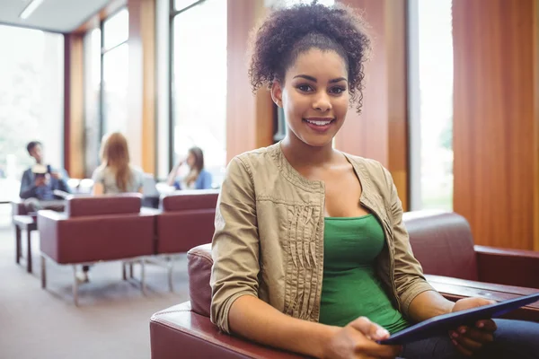 Student sitting on sofa using her tablet pc smiling at camera — Stock Photo, Image