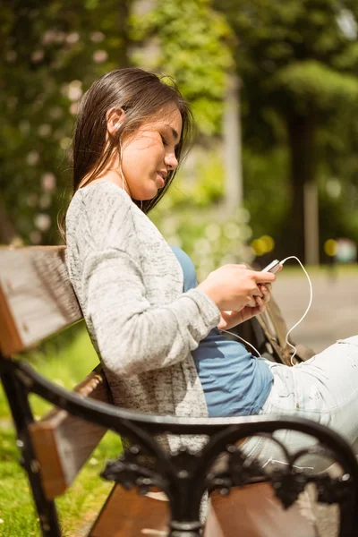 Улыбающаяся студентка, сидящая на скамейке для смс на мобильном телефоне — стоковое фото