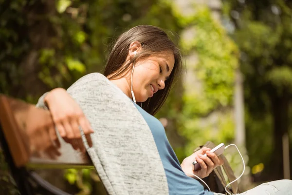 Estudiante sonriente sentada en el banco mensaje de texto en su teléfono móvil — Foto de Stock