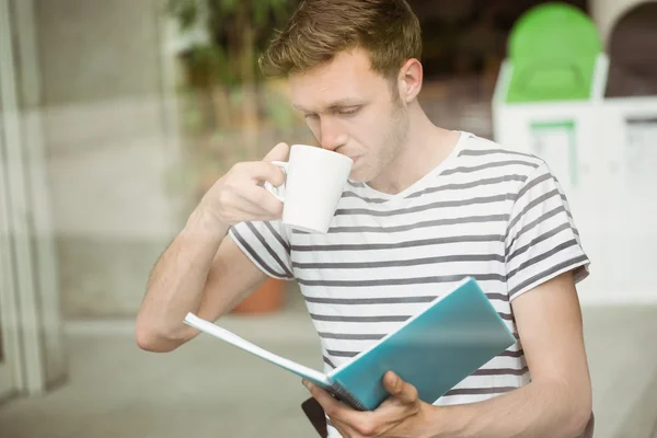 Student trinkt ein Heißgetränk und hält Buch in der Hand — Stockfoto