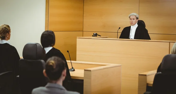 Unsmiling judge wearing wig with american flag behind him — Stock Photo, Image