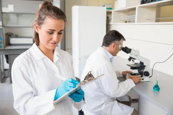 Junge Wissenschaftlerin schreibt auf Klemmbrett — Stockfoto