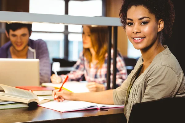 Studentin sitzt am Schreibtisch und schreibt auf Notizblock — Stockfoto