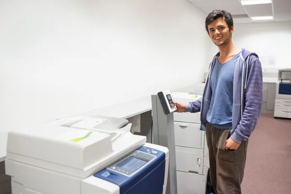 Estudante sorrindo de pé ao lado da fotocopiadora — Fotografia de Stock
