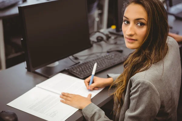 Lächelnder Student sitzt am Schreibtisch und schreibt auf Notizblock — Stockfoto