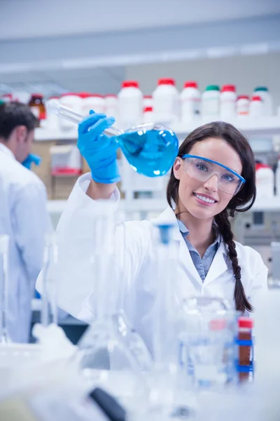 Портрет улыбающегося химика, держащего стакан с голубой жидкостью — стоковое фото