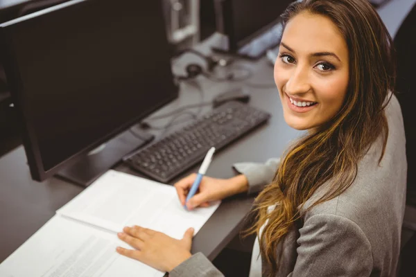 Lächelnder Student sitzt am Schreibtisch und schreibt auf Notizblock — Stockfoto