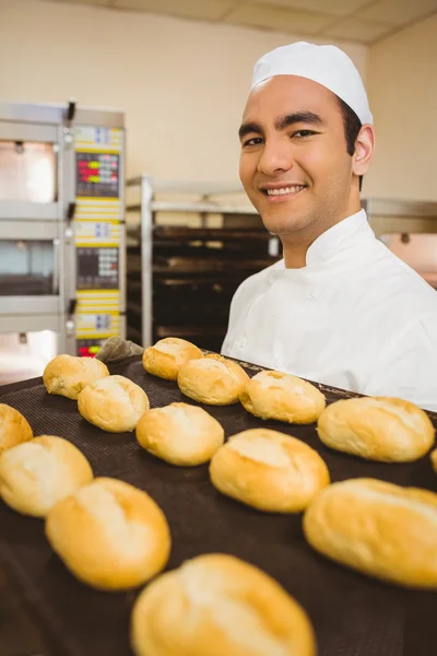 Bäcker lächelt in Kamera und hält Tablett mit Brötchen — Stockfoto