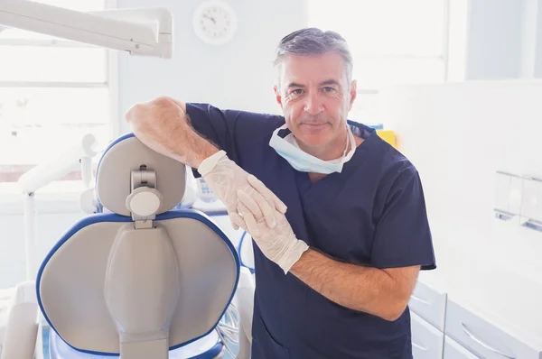 Улыбающийся дантист опирается на стул стоматолога — стоковое фото