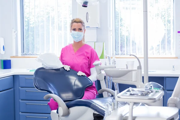 Dentista en máscara mirando a la cámara al lado de la silla —  Fotos de Stock