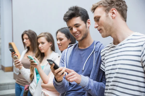 Los estudiantes que utilizan sus teléfonos inteligentes en una fila —  Fotos de Stock