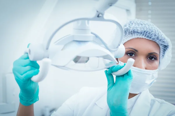 Dentista femenina en máscara quirúrgica ajustando la luz — Foto de Stock