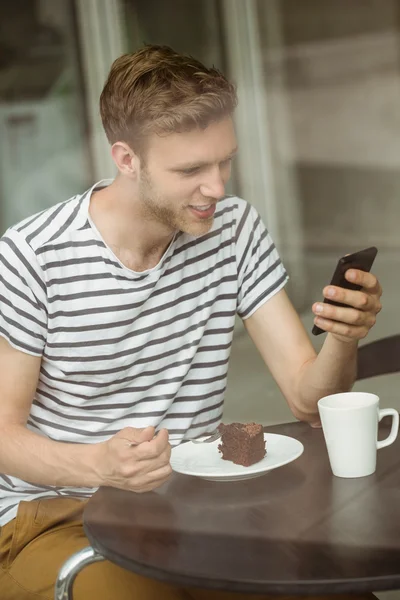 Usměvavý student s čokoládový dort pomocí smartphone — Stock fotografie