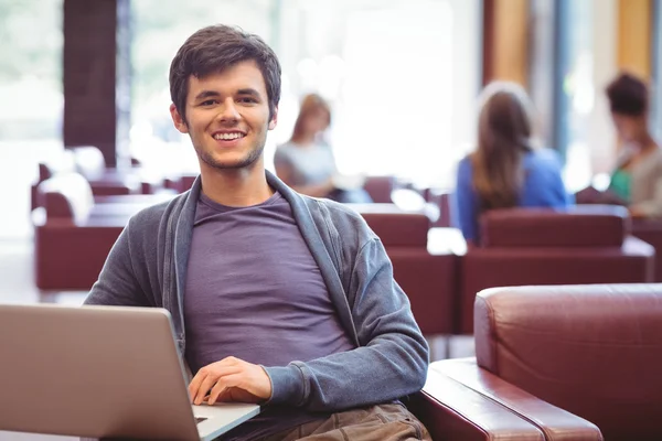 Glad ung student sitter på soffan med laptop — Stockfoto