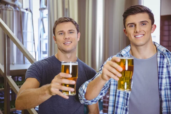 Young men holding a pint of beer smiling at camera — Stock Photo, Image