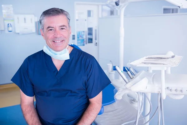 Dentista sonriendo a la cámara junto a la silla — Foto de Stock