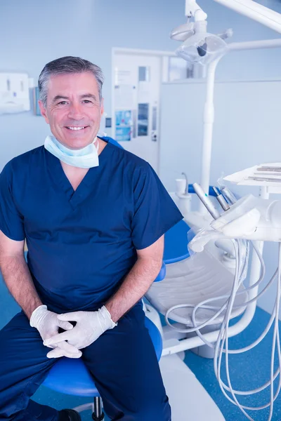 Lachende tandarts in blauw scrubs zittend in stoel — Stockfoto