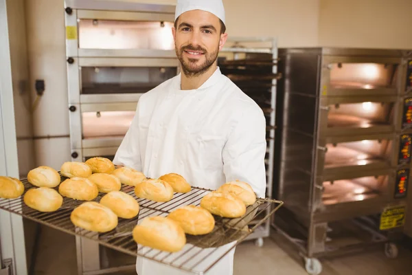 Baker sorridente alla macchina fotografica che tiene rack di rotoli — Foto Stock