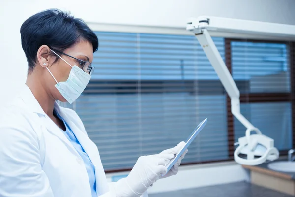 Dentista em máscara cirúrgica usando tablet digital — Fotografia de Stock