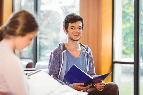 Students sitting on couch revising and smiling at camera — Stock Photo, Image