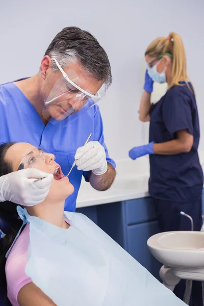 Dentista vestindo protetor facial e examinando um paciente — Fotografia de Stock