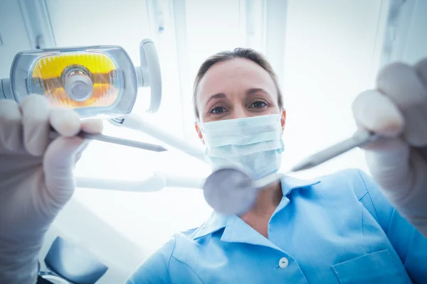 Dentista feminina em máscara cirúrgica segurando ferramentas dentárias — Fotografia de Stock