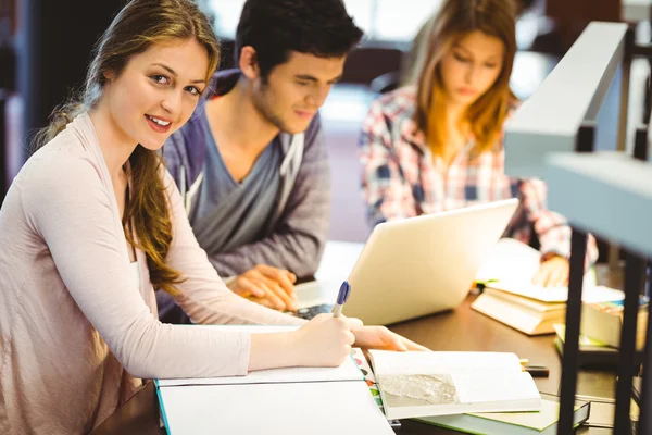 Gelukkig student schrijven op haar notitieblok glimlachen op camera — Stockfoto