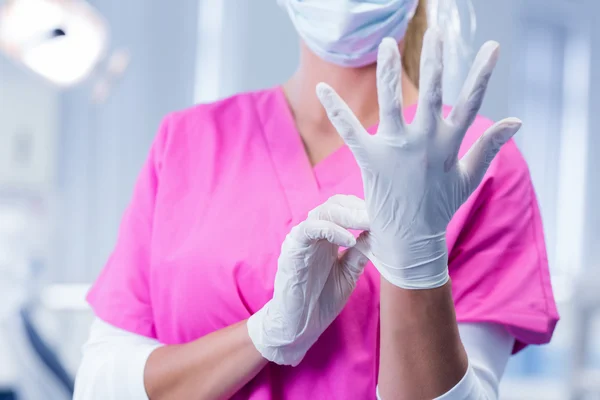 Tandarts in roze scrubs zetten chirurgische handschoenen — Stockfoto