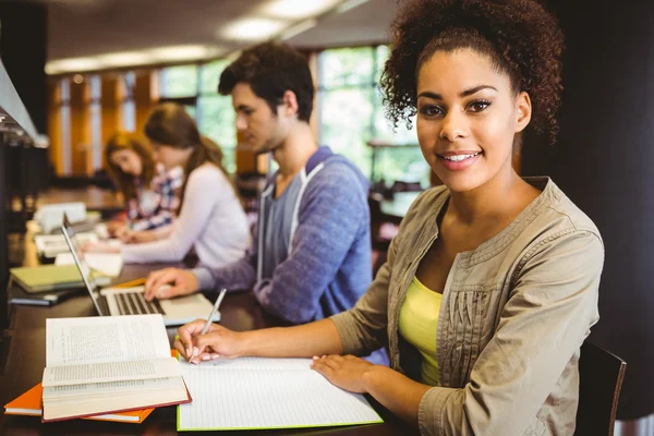 Student looking at camera while studying with classmates — Stock Photo, Image