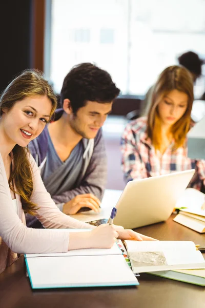 Feliz estudiante escribiendo en su bloc de notas sonriendo a la cámara — Foto de Stock