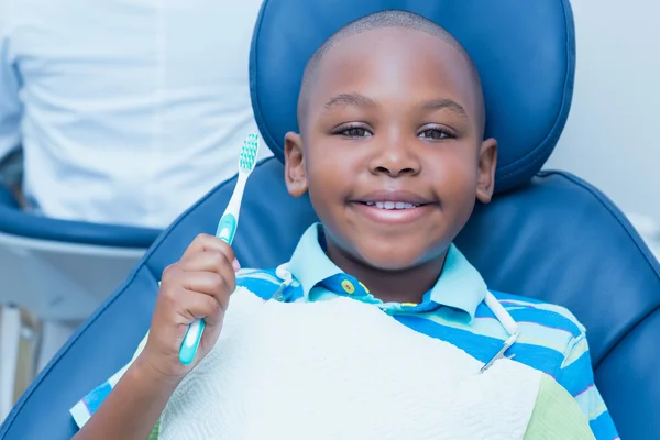 Niño sosteniendo cepillo de dientes en la silla de dentistas — Foto de Stock