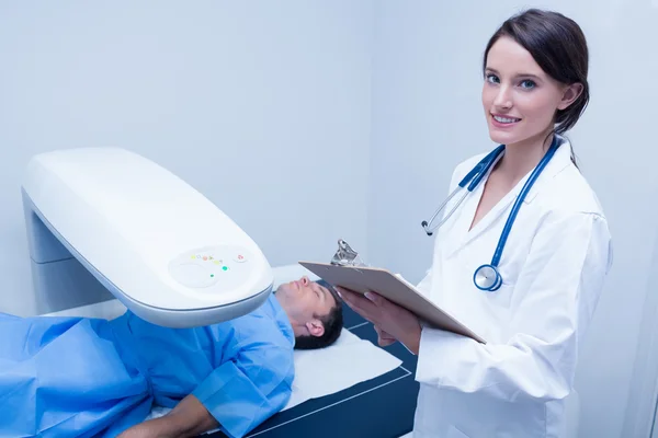 Doctor writing on clipboard while looking at camera — Stock Photo, Image